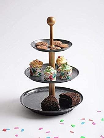 A three-tier metal cake stand with black and copper finish, displaying cupcakes on each tier, placed on a white surface with confetti scattered around.