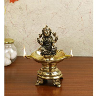 A traditional Indian brass diya with a sculpture of goddess Lakshmi sitting on a lotus base, designed for use as a oil lamp.