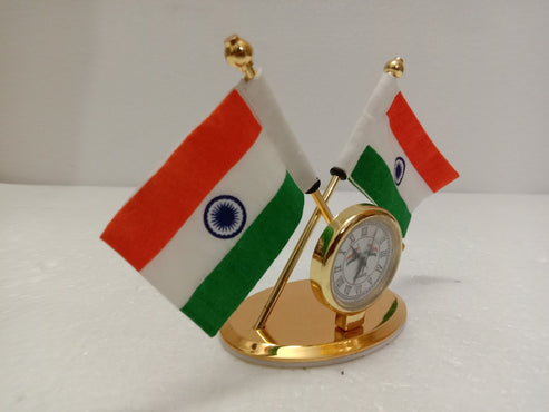 A small gold-colored desk clock featuring two miniature Indian flags on a white surface against a plain light gray background.