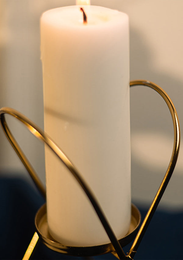 White candle in a gold holder against a neutral background