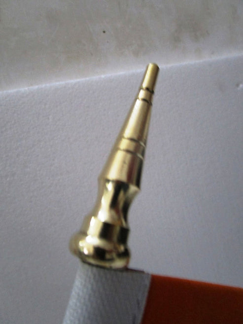 Close-up of a metallic gold brass nozzles tip on a white textured background with a red surface visible at the bottom right.