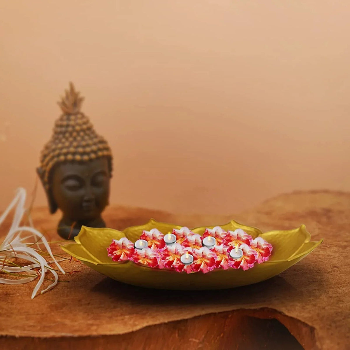 A golden, lotus-shaped iron bowl with delicate petal detailing, displayed on a textured background with a sculpture of a Buddha in the background.