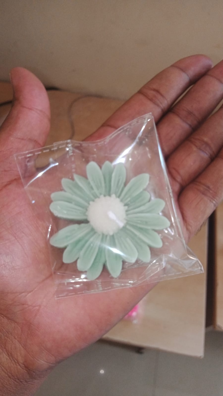 Light green flower-shaped candle in a clear plastic bag held by a hand.