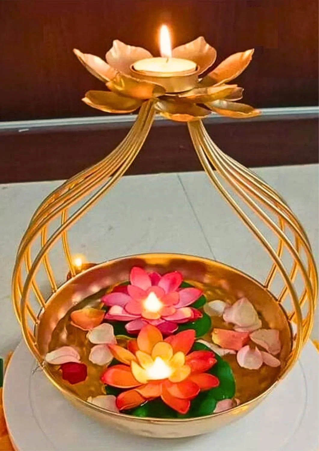 A decorative golden lotus-shaped candle holder stands above a shallow bowl filled with water.