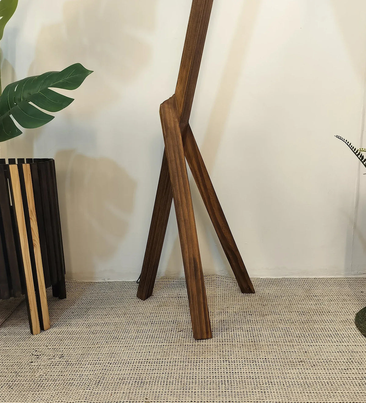 Wooden plant stand with a plant on a textured floor against a neutral wall