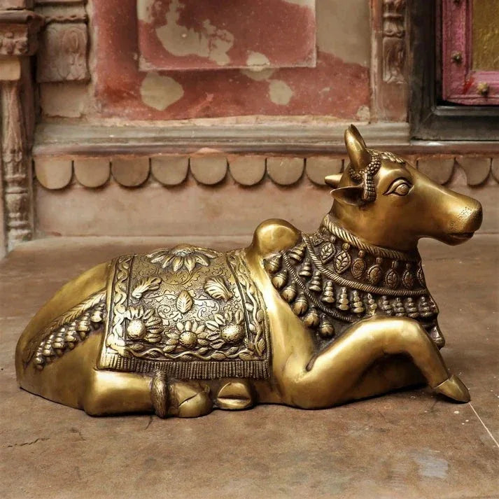 Decorative brass sculpture of a cow with intricate designs on a stone floor.