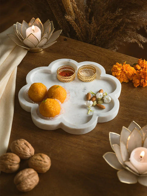 Decorative marble tray with fruits and nuts on a wooden surface with candles and flowers.