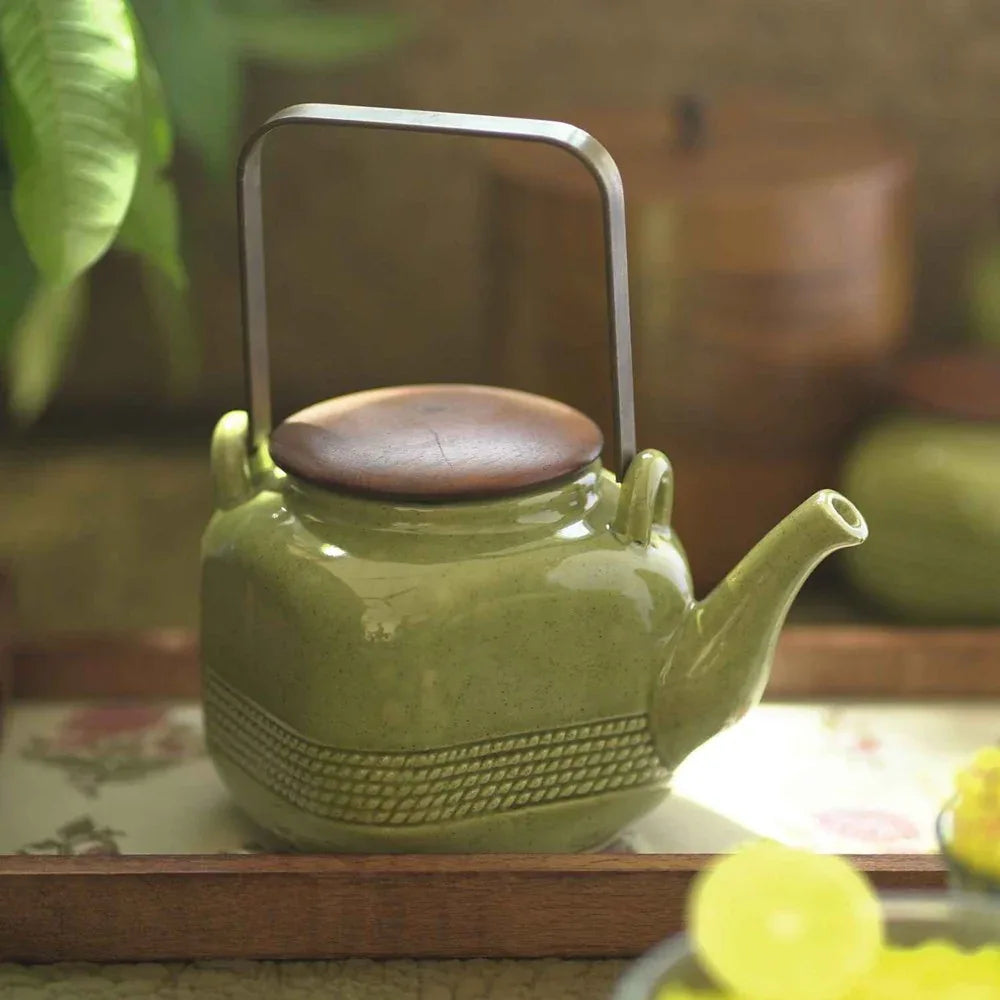Green ceramic teapot with a brown lid on a wooden surface