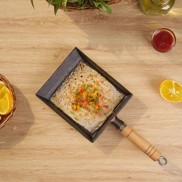 Small frying pan with food on a wooden table with oranges and a plant.