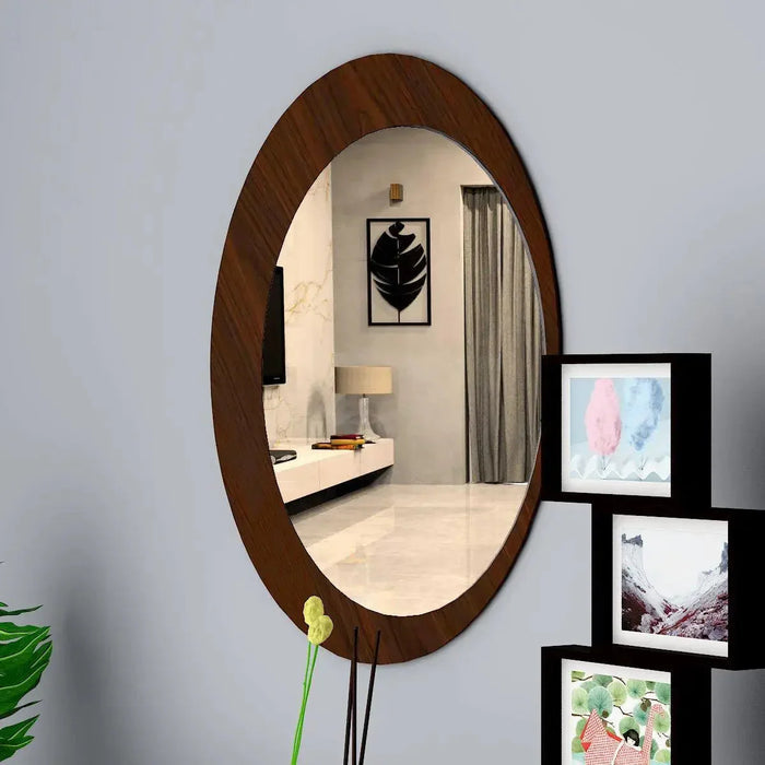 Wooden oval mirror on a wall with framed pictures below