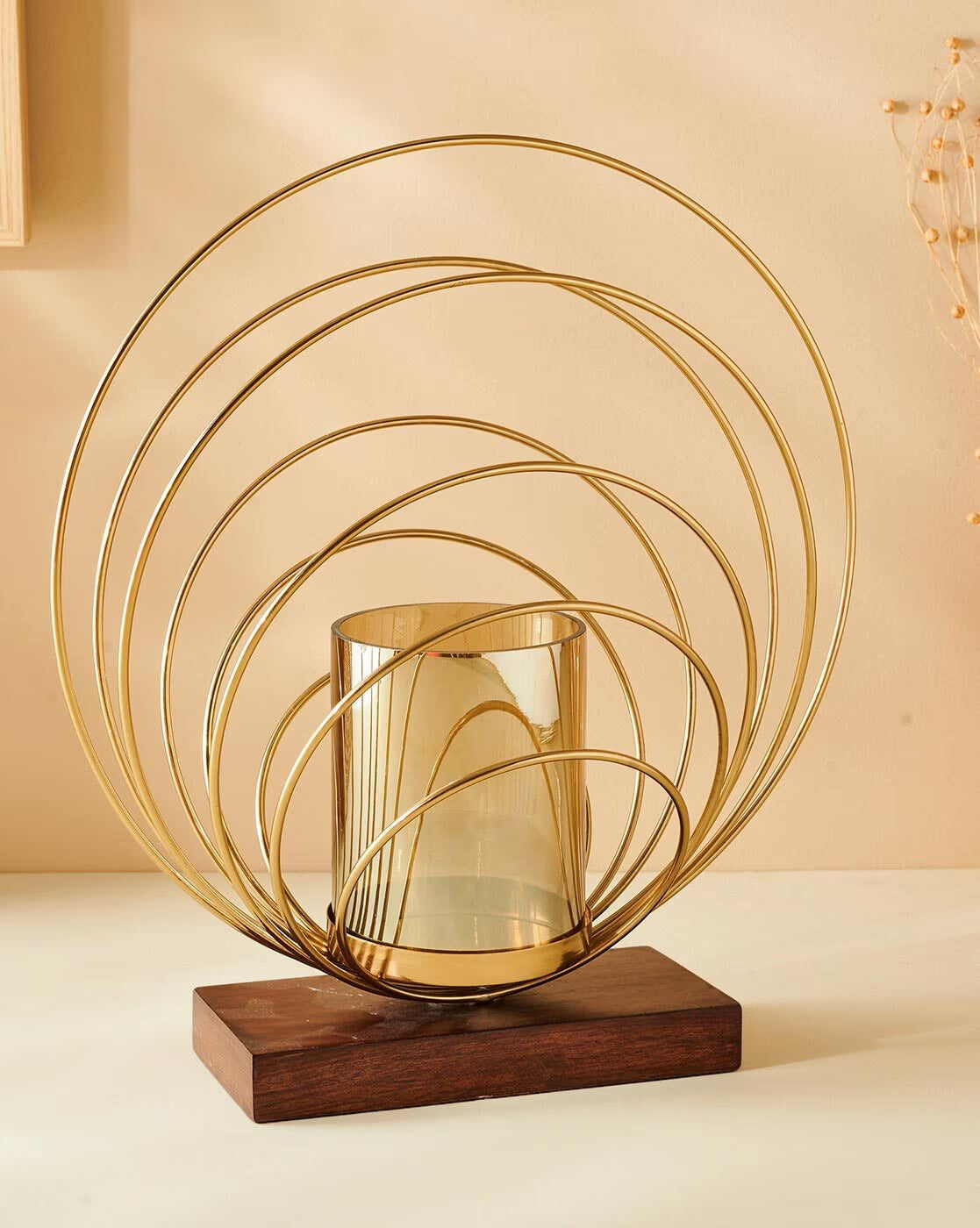 Decorative gold metal sculpture with a glass container on a wooden base against a beige background