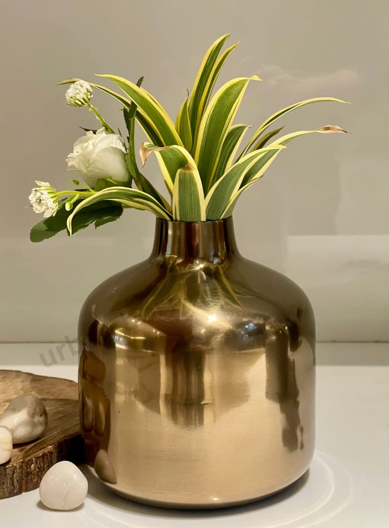 Bronze vase with green plant and white flowers on a neutral background