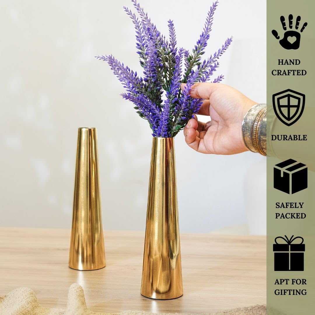 Gold vase with lavender being held, next to a hand holding a gold vase, on a wooden surface.