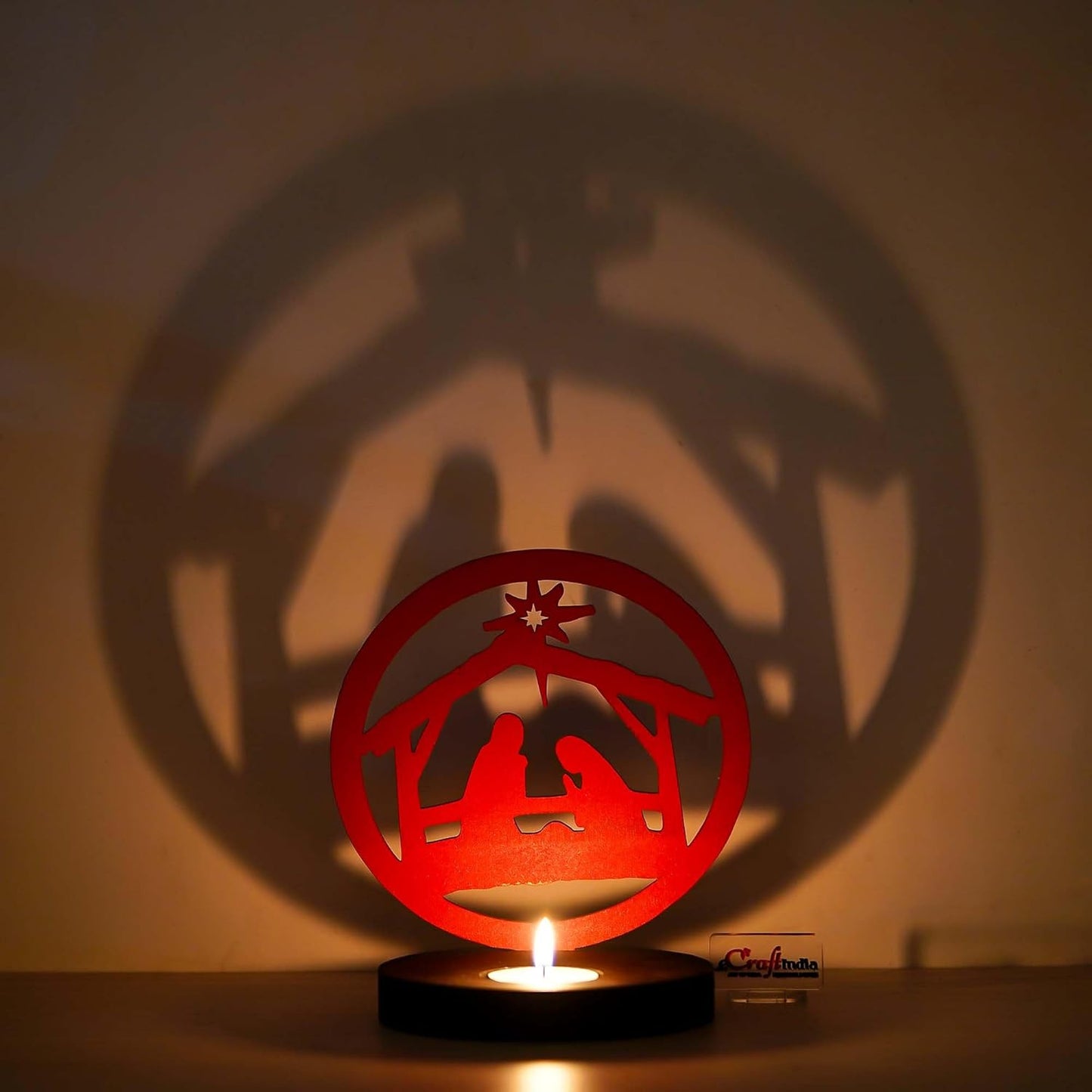Red nativity scene cutout casting a shadow on a wall with a lit candle