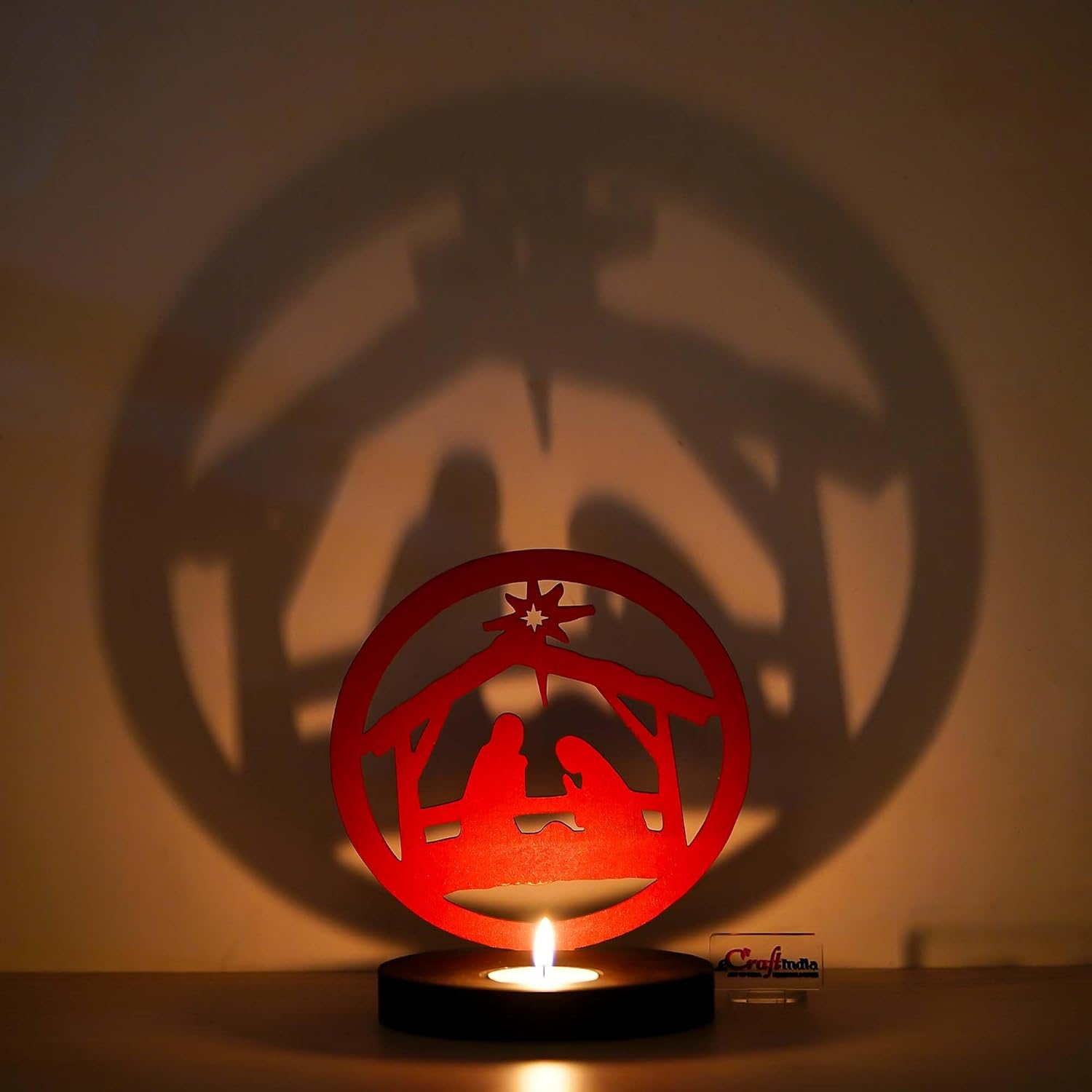 Red nativity scene cutout casting a shadow on a wall with a lit candle