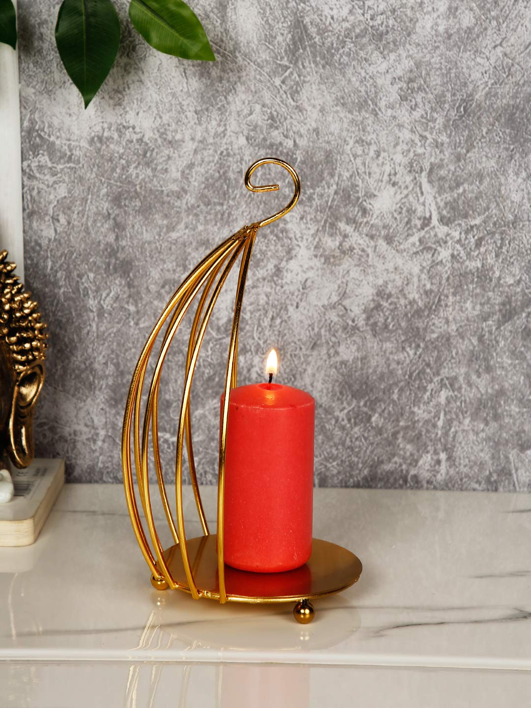 Red candle in a gold holder on a marble surface with a gray textured wall background