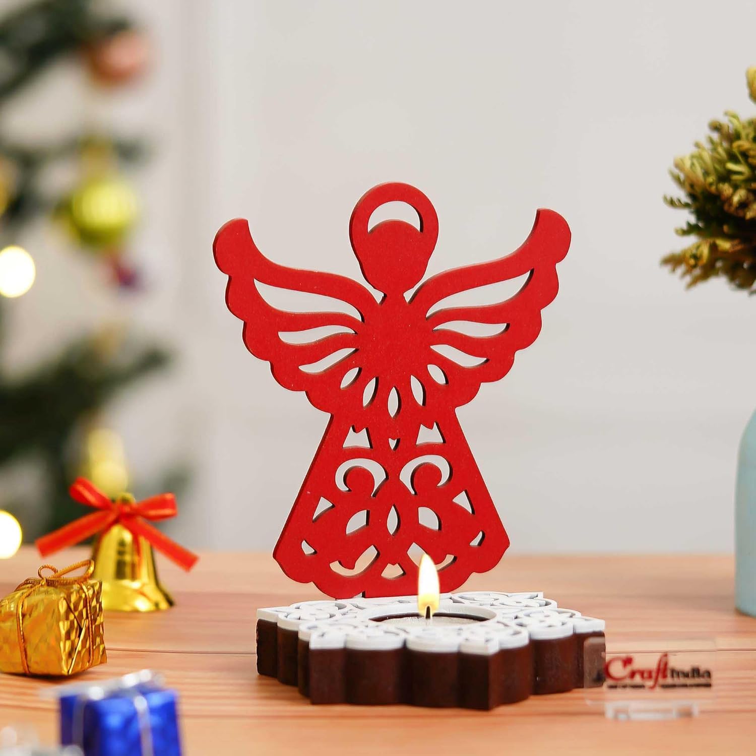 Red angel-shaped candle holder on a wooden surface with blurred Christmas decorations
