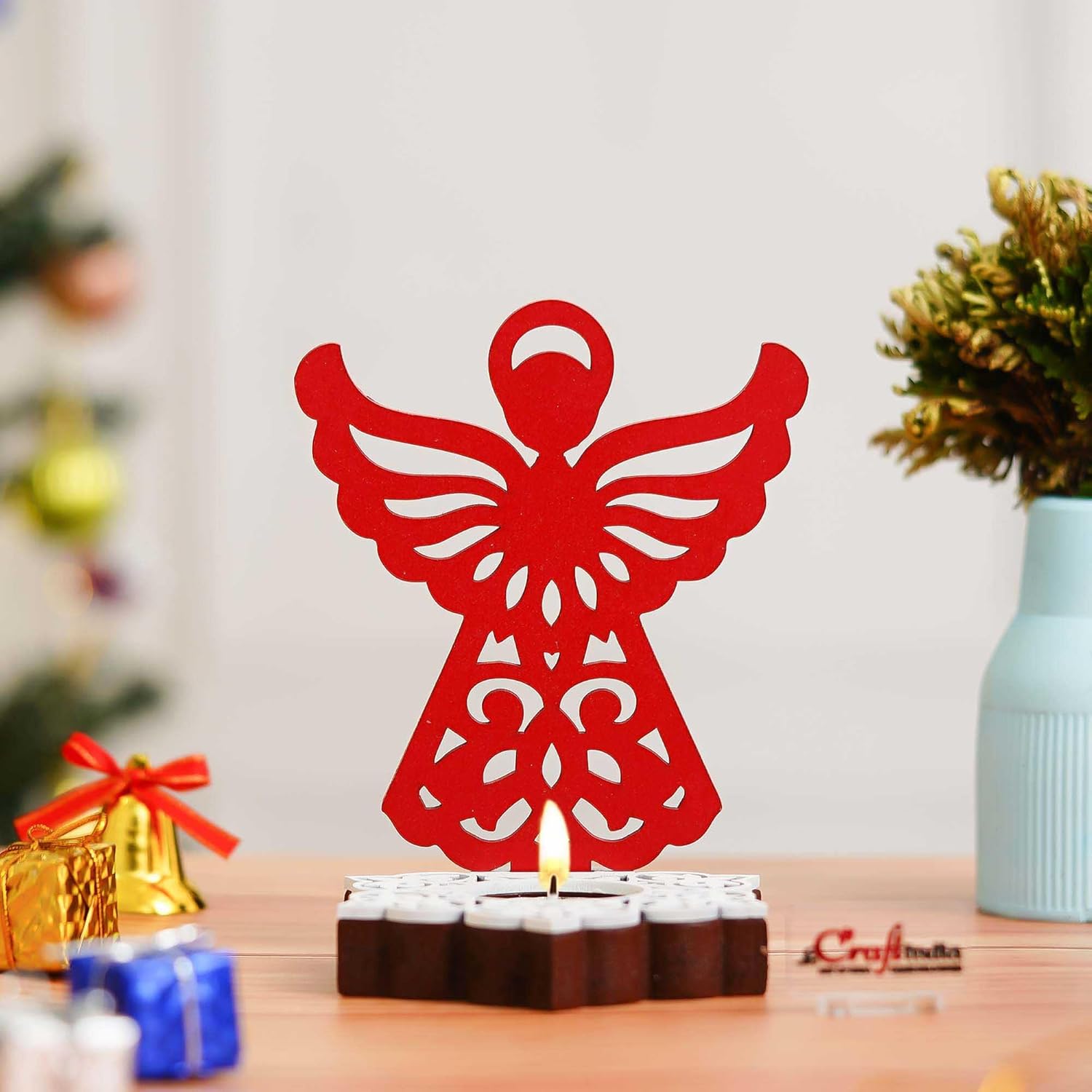Red angel-shaped candle holder on a table with blurred decorative items