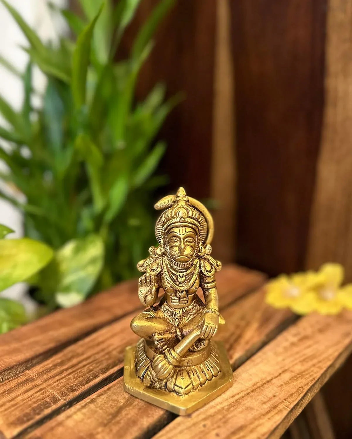 Hanuman brass statue of a seated figure on a wooden surface with plants in the background