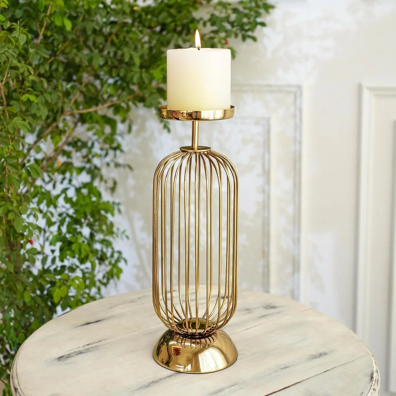 Gold candle holder with a white candle on a marble surface, with greenery in the background.
