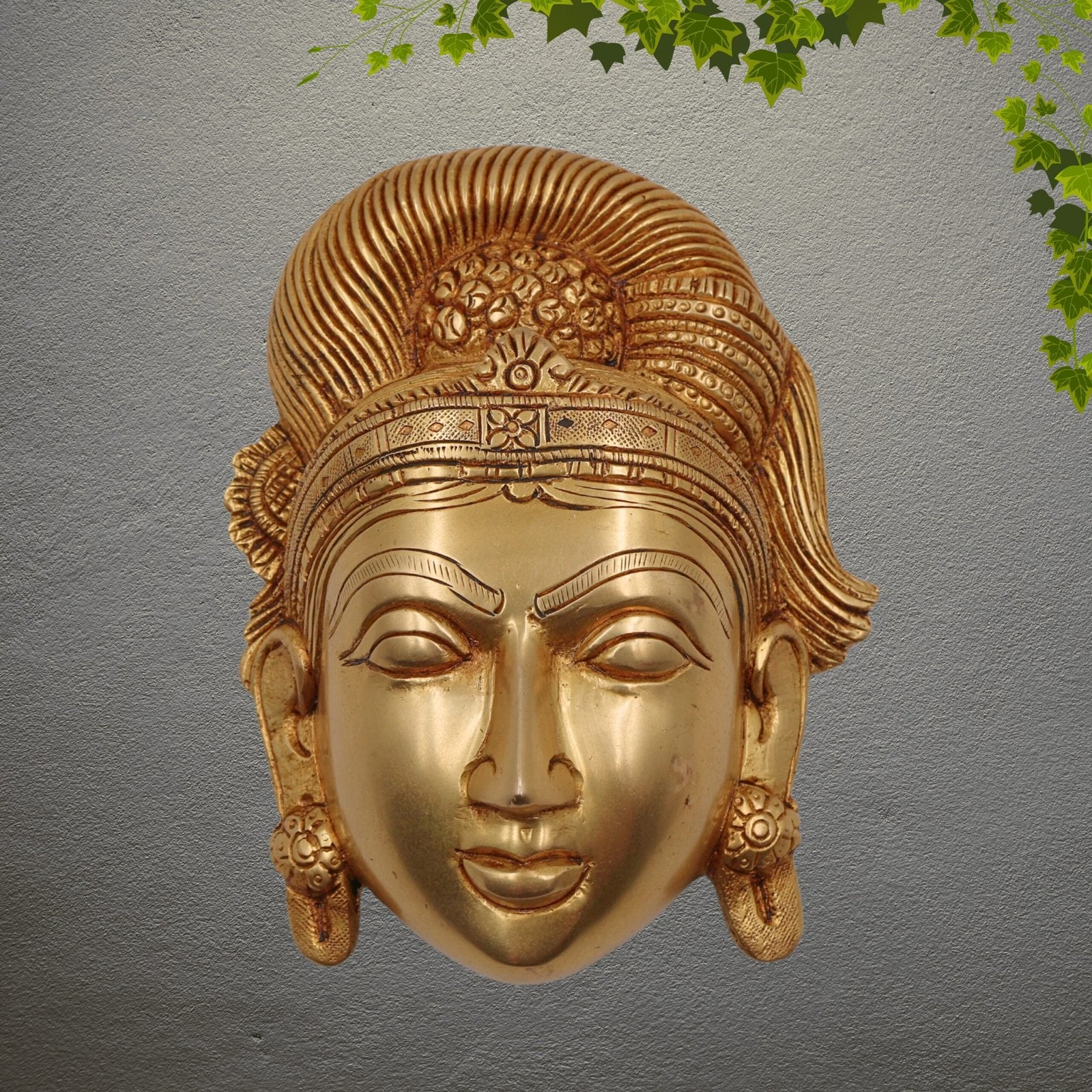 Gold decorative mask on a gray background with green leaves at the top.