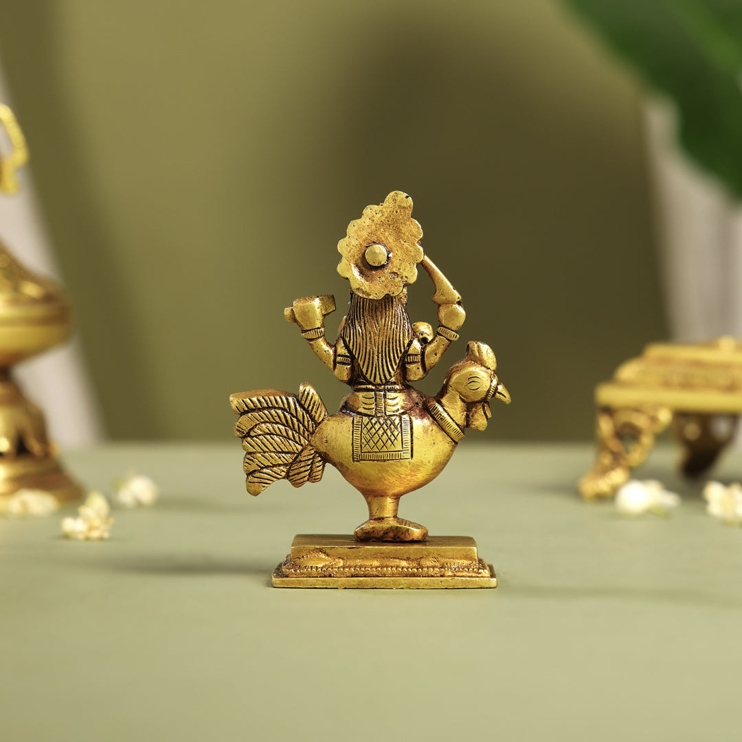 Gold figurine of goddess parvathi riding a rooster on a green surface