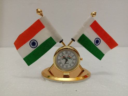 A small gold desk clock with Roman numerals, featuring two miniature Indian flags on gold poles that curve around the clock, set against a plain light background.
