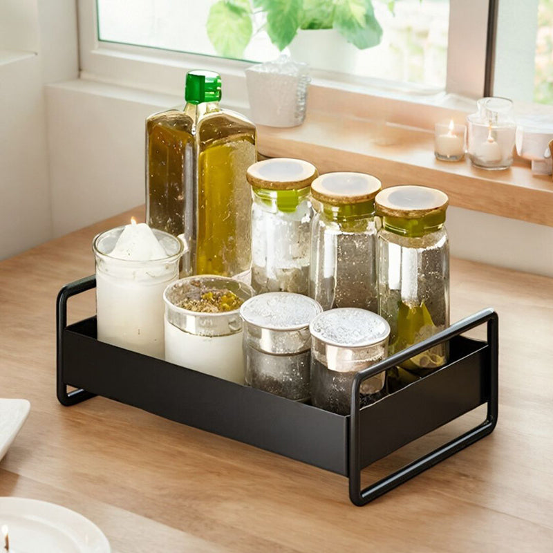 Decorative items including bottles, jars, and candles on a black tray in a bright room.