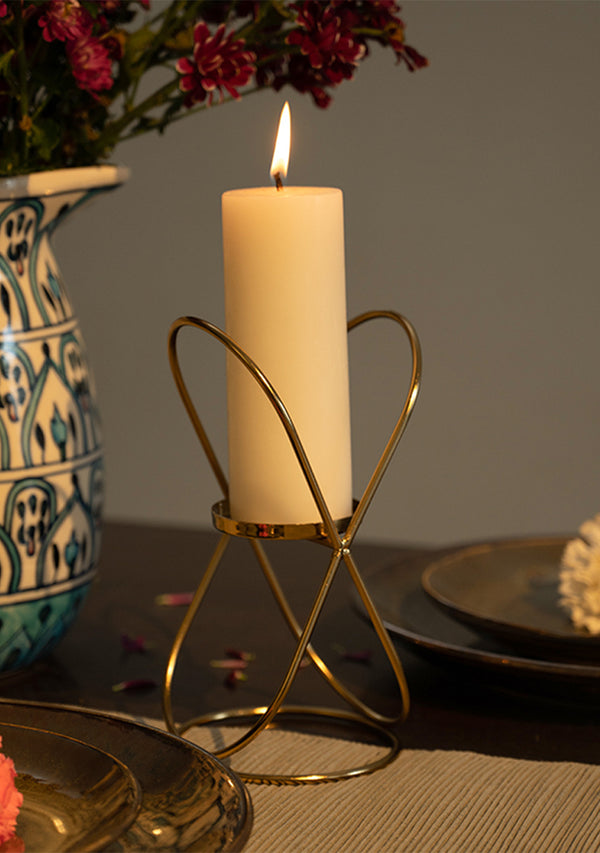 Candle in a decorative holder on a table with a vase and flowers in the background