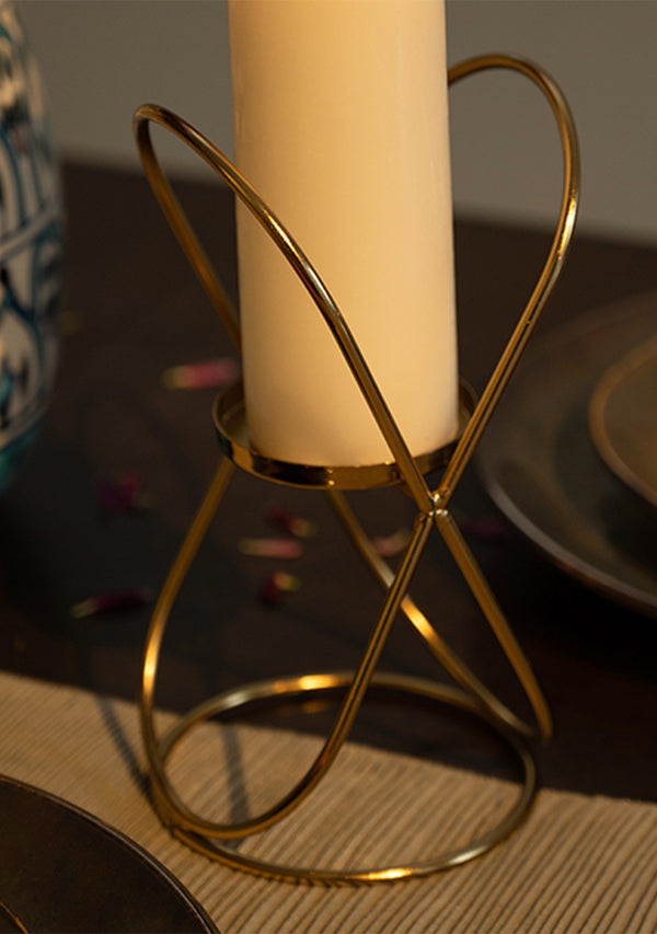 Gold candle holder with a white candle on a textured surface