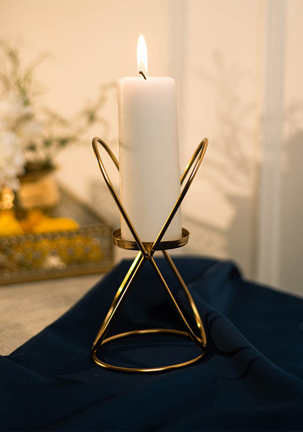 White candle in a gold holder on a dark surface with a blurred background