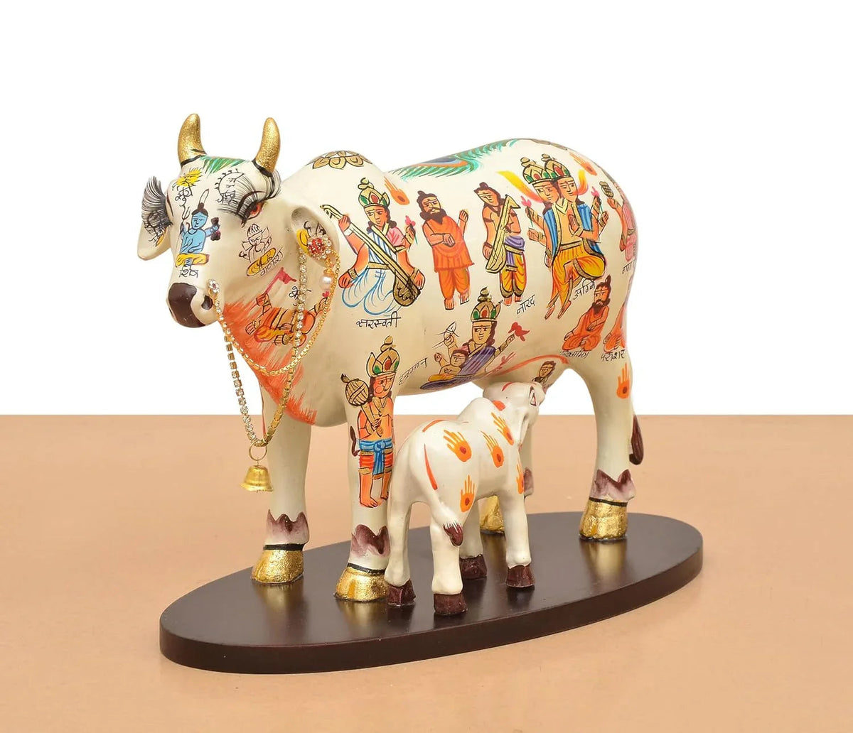 Handcrafted 8-inch resin Kamdhenu cow with calf — hand-painted multicolour with Hindu deities and saints including Hanuman, Narad, Saraswati and sages, gold hooves and brass bell chain — ArtyCraftz