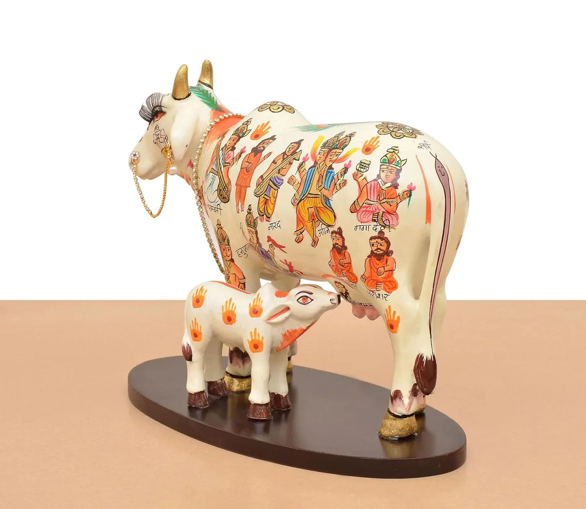 Handcrafted 8-inch resin Kamdhenu cow with calf — hand-painted multicolour with Hindu deities and saints including Hanuman, Narad, Saraswati and sages, gold hooves and brass bell chain — ArtyCraftz