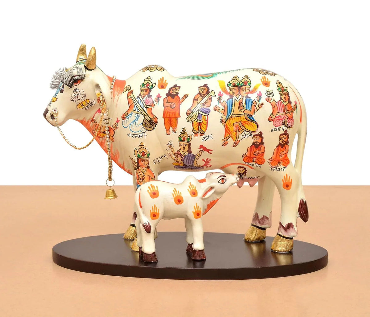 Handcrafted 8-inch resin Kamdhenu cow with calf — hand-painted multicolour with Hindu deities and saints including Hanuman, Narad, Saraswati and sages, gold hooves and brass bell chain — ArtyCraftz
