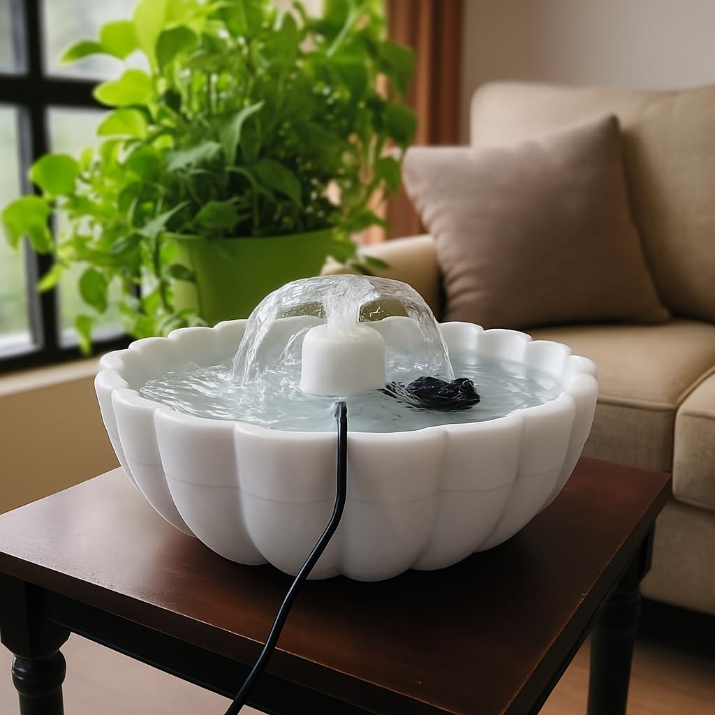 White ceramic water fountain on a wooden table with a couch and plant in the background