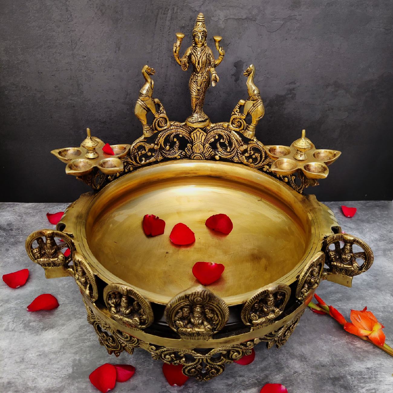 Decorative gold tray with statues and red flower petals on a gray background