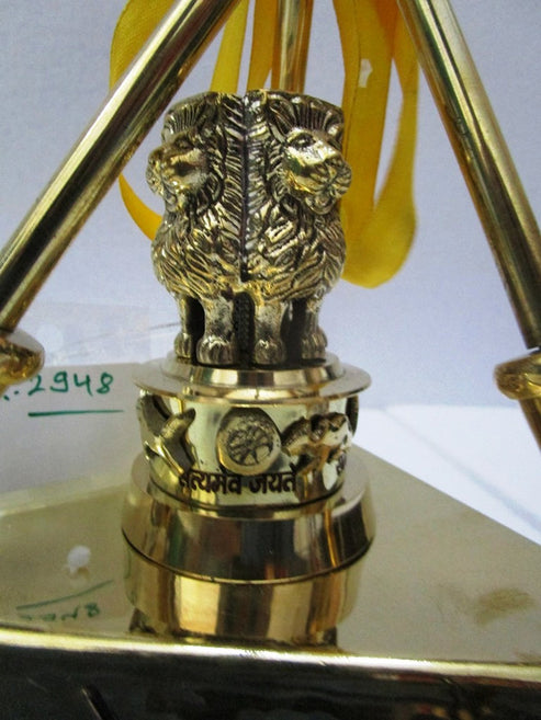 A close-up of a brass Lord Hanuman statue on a pedestal, featuring the name 'Sri Lakshmi Yantra' engraved on the base, with yellow ribbons attached behind it.
