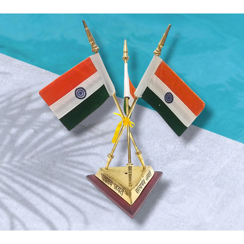 A decorative miniature Indian desk flag set featuring two small Indian flags mounted on gold-colored crossed poles, tied with a yellow ribbon, and mounted on a triangular gold base with Hindi text, set against a split white and turquoise background.