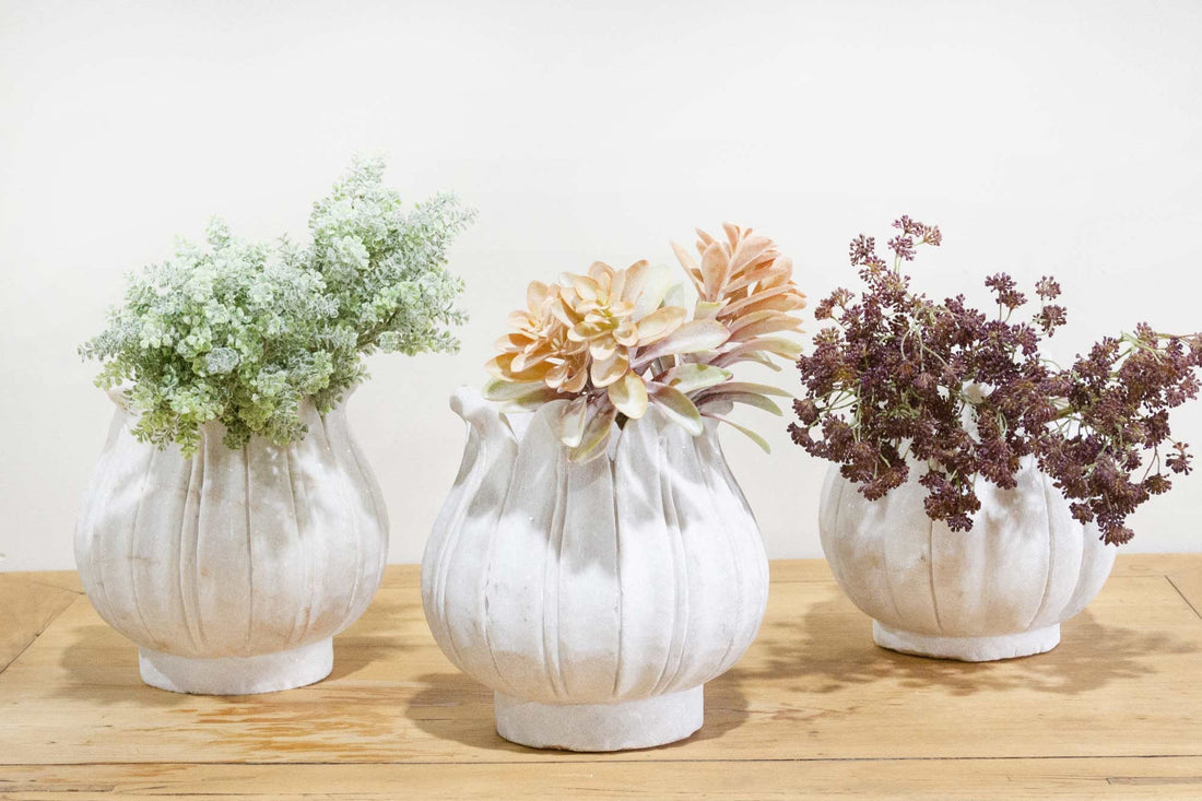 Three white ceramic vases with floral arrangements on a wooden surface.