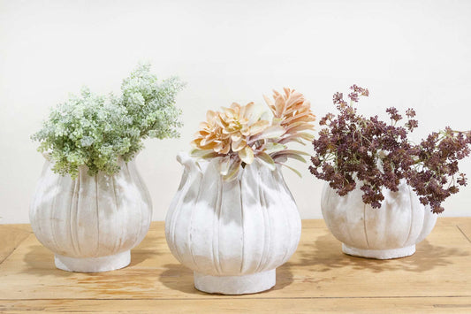 Three white ceramic vases with floral arrangements on a wooden surface.