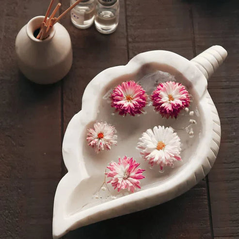 Decorative leaf-shaped bowl with floating flowers on a wooden surface