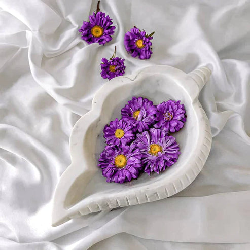 Purple flowers in a white decorative dish on a white fabric background