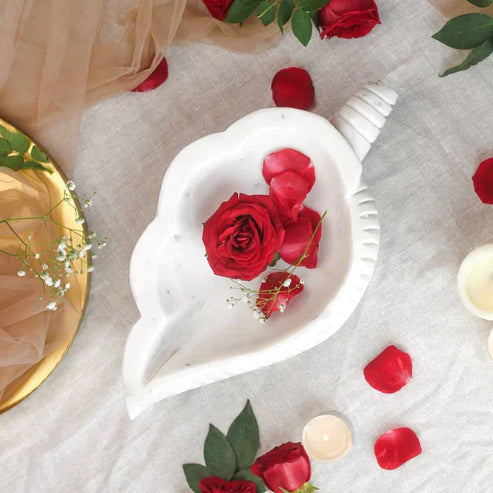 Heart-shaped white dish with red roses on a light gray surface with scattered rose petals.