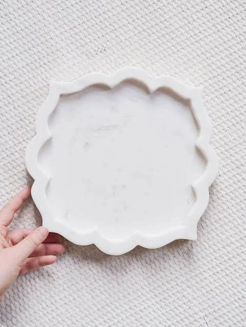 White scalloped-edge ceramic plate held by a hand on a textured gray surface