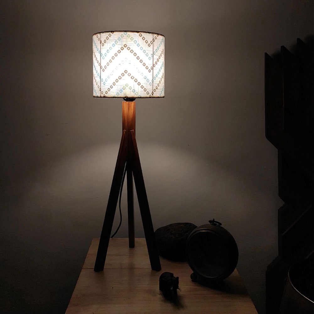Floor lamp with patterned shade on a wooden platform against a dark wall