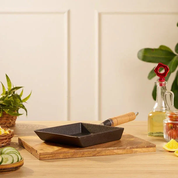 Black frying pan on a wooden cutting board with a plant and bottles