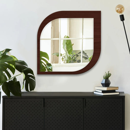 Square mirror with wooden frame on a white wall above a black cabinet with decorative items.