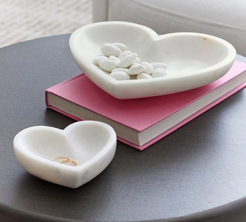 Heart-shaped ceramic bowls with small stones and a ring on a pink book