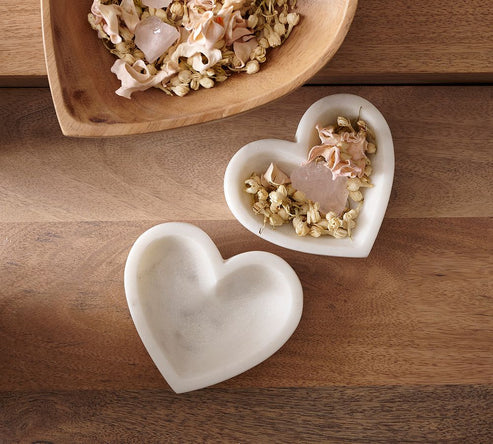 Two heart-shaped white ceramic dishes on a wooden surface with dried flowers and a pink stone.