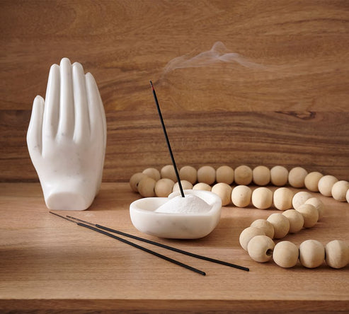 White marble hand sculpture, incense sticks, and wooden beads on a wooden surface.